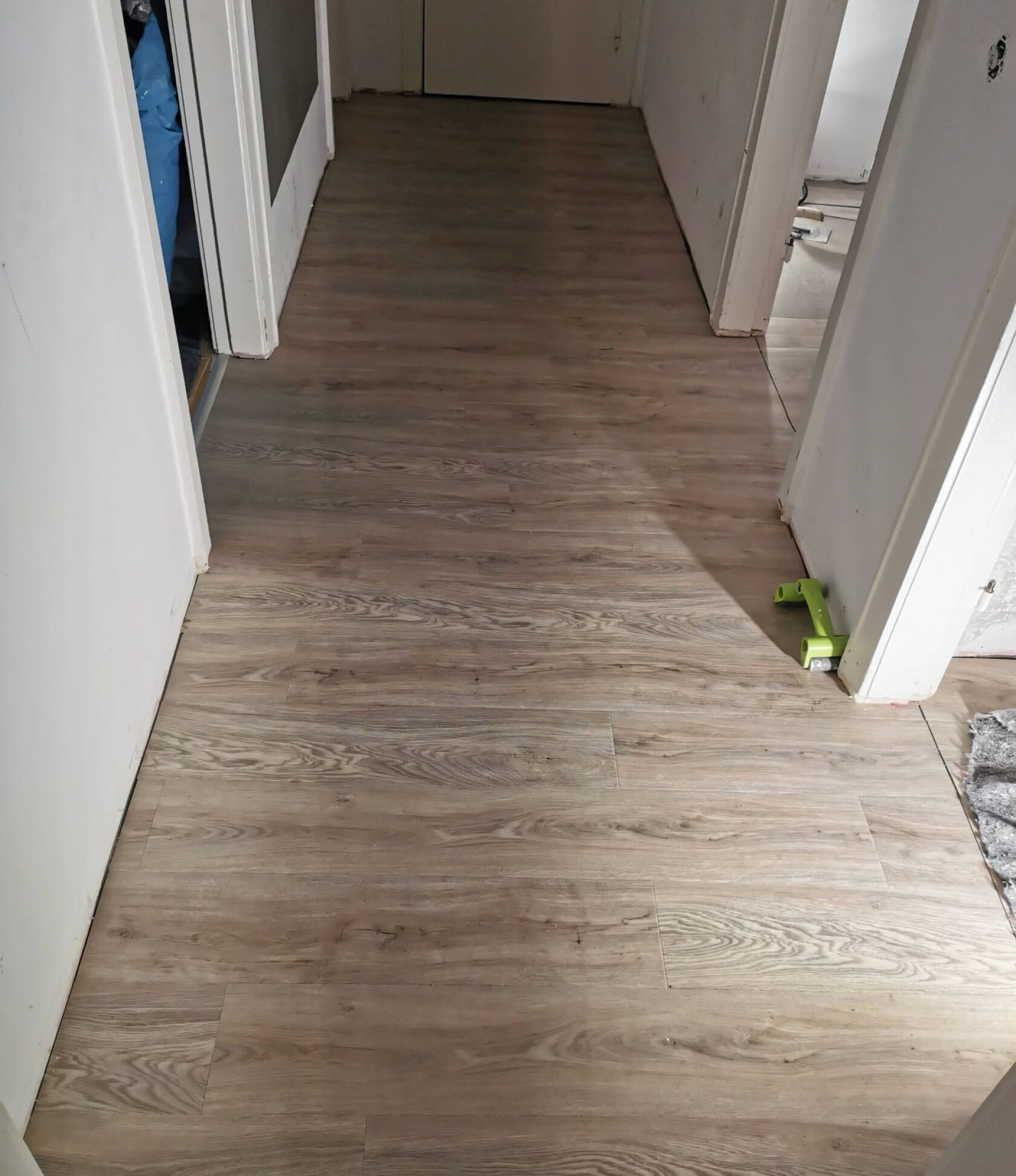 Laminatdielen mit hellbraunem Holzmaserungsdekor, verlegt in einem schmalen Flur; weiße Türzargen links und rechts, rechterseits ein grüner Kunststoff-Abstandhalter an der Türschwelle.