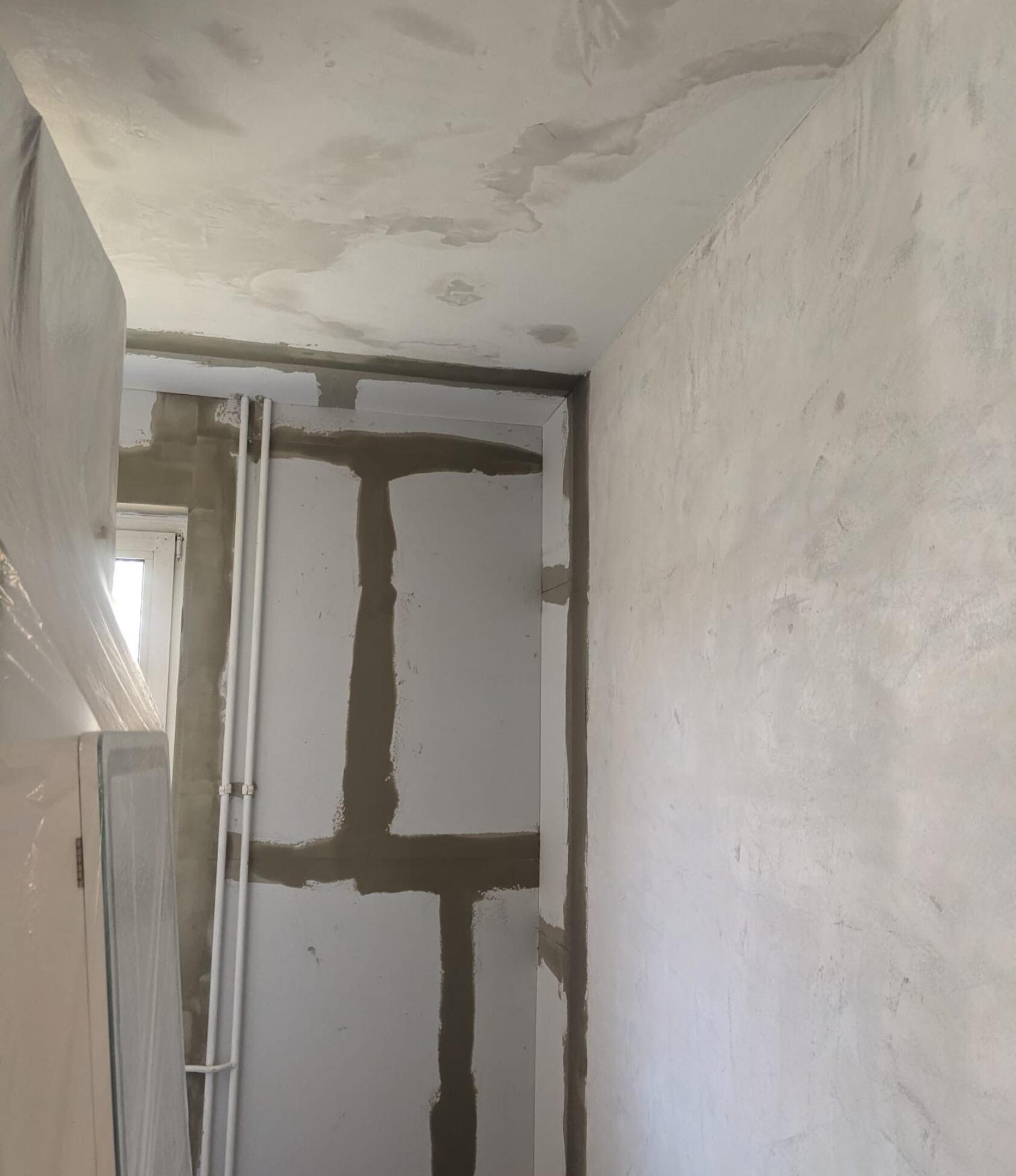 Raumecke – gespachtelte Fugen bilden an der linken Wand ein dunkles Kreuzmuster, zwei senkrechte weiße Rohrleitungen, fleckige Decke mit Verfärbungen, rechts glatter Putz.