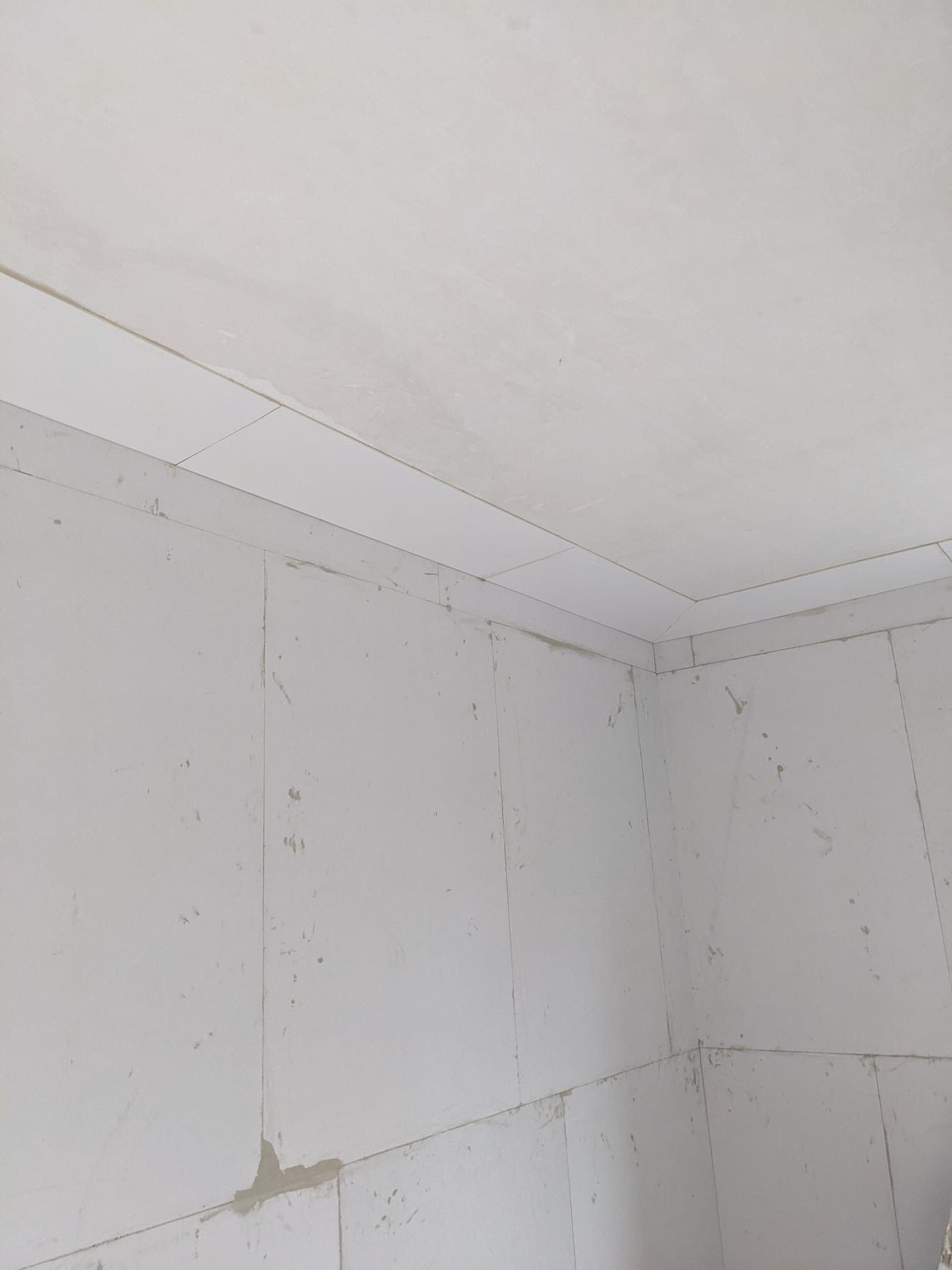 Ecke eines weißen Rohbauzimmers: Gipskartonwände und Deckenplatten treffen sich, sichtbare Nähte und Fugen, schmutzige Flecken und Putzspuren an den Wandflächen.
