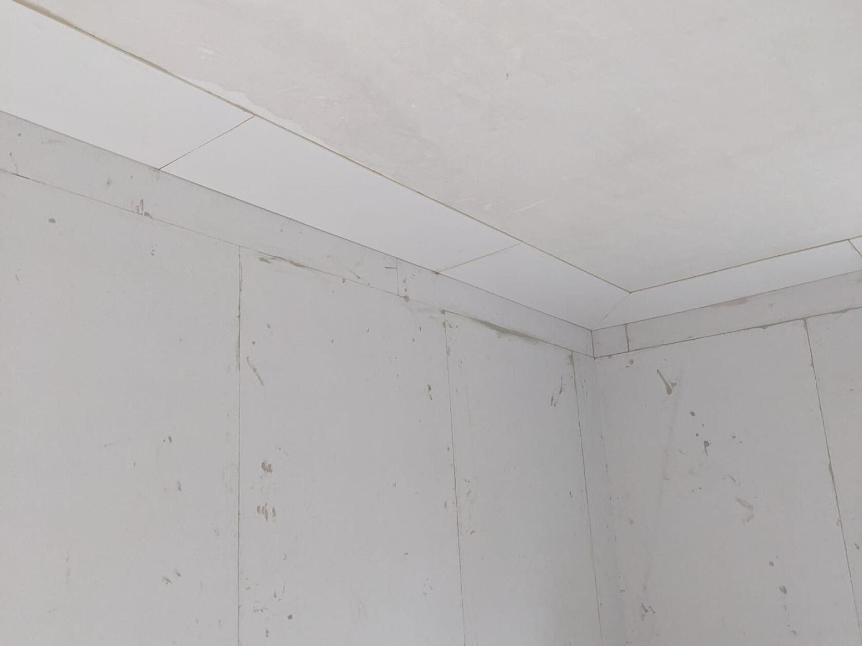 Ecke eines weißen Rohbauzimmers: Gipskartonwände und Deckenplatten treffen sich, sichtbare Nähte und Fugen, schmutzige Flecken und Putzspuren an den Wandflächen.