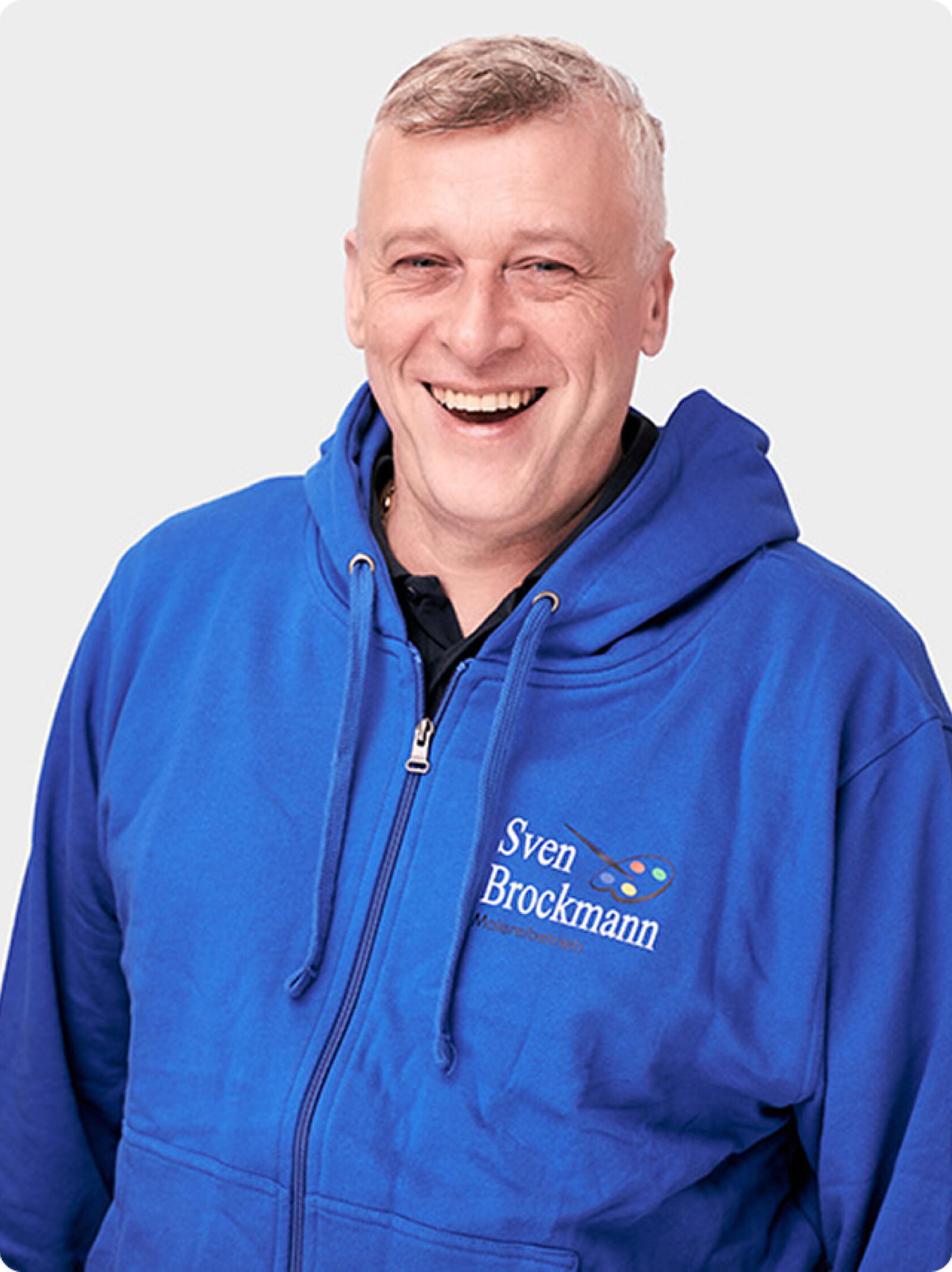 Erwachsener Mann lächelt, trägt blaue Kapuzenjacke mit aufgedrucktem Text 