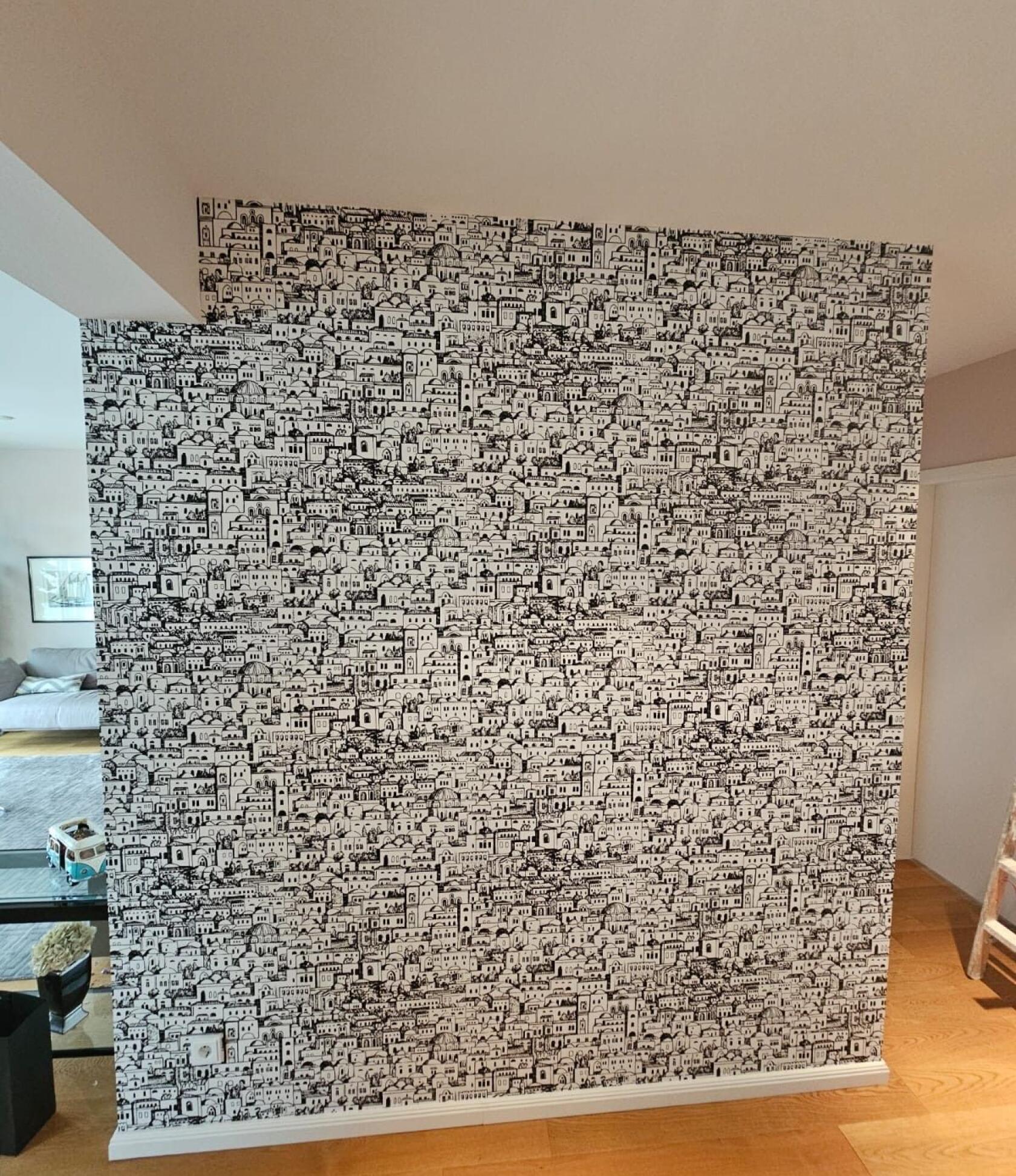 Innenwand, bedeckt mit dicht gezeichnetem schwarz-weißem Stadtmuster auf Tapete, im Wohnraum; sichtbarer Holzboden, weiße Sockelleiste, Sofa und kleines Spielzeug links, Leiter rechts.