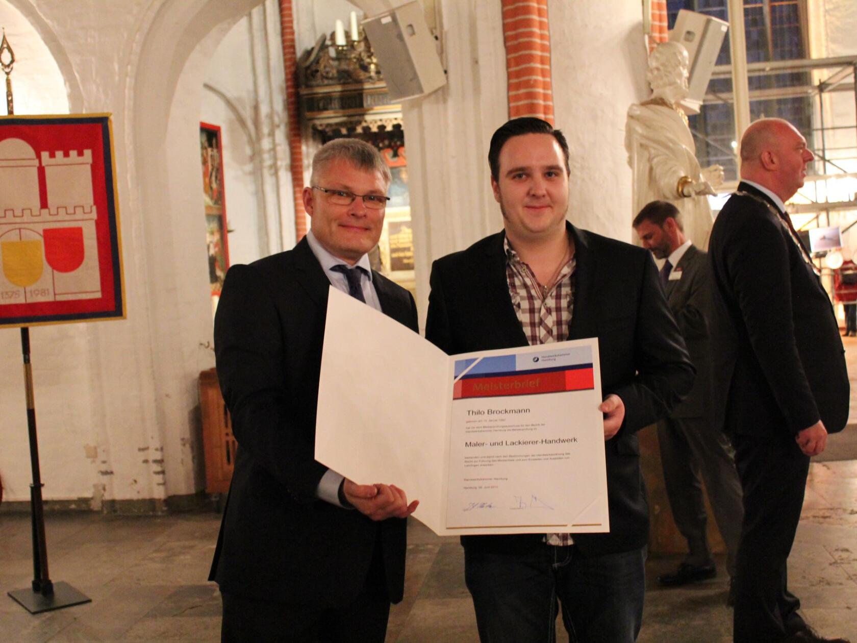 Zwei Männer halten eine geöffnete Urkunde mit Titel 
